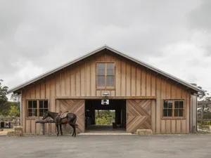 Industrial-style barn with wooden exterior and large doors, featuring a horse standing outside.