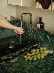 Person washing hands in a modern bathroom with a green marble countertop and a bottle of mouthwash.