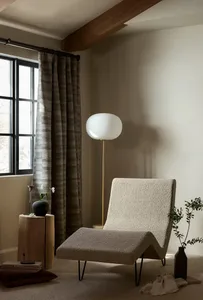 Modern minimalist living room with a textured fabric lounge chair, a floor lamp with a spherical shade, and a small plant.