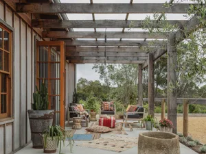 Rustic outdoor living room with wooden pergola, fabric seating, and stone accents.