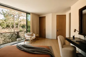 Modern minimalist bedroom featuring wood flooring, furniture, and doors with large windows overlooking nature.
