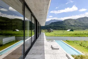 Modern residential house featuring sleek concrete and glass architecture with a poolside view of green fields and mountains i