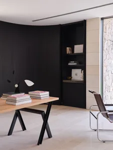 A modern, minimalist home office featuring a black metal and wood desk with books and a lamp, alongside a sleek, minimalist a