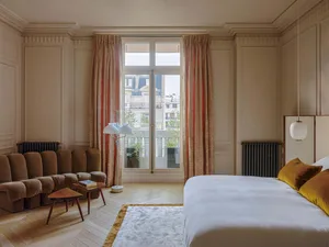 A modern bedroom with a large window, comfortable seating area, and a cozy bed.