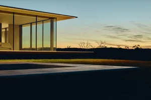 A modern minimalist residential exterior featuring large glass windows and wooden structural elements at sunset.