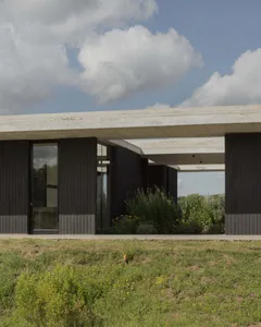 Modern residential exterior featuring concrete pillars and dark panels with glass doors.