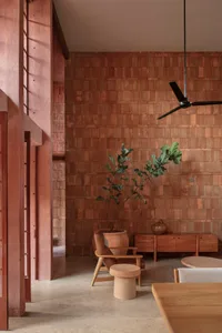 Minimalist living room featuring red brick walls and floor, a wooden dining table, and a hanging black ceiling fan.