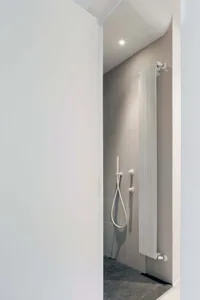 Modern minimalist bathroom featuring ceramic tiles flooring and walls, with a sleek white radiator and simple fixtures.