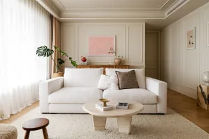 A minimalistic living room with a white couch, neutral-toned rugs, and a round coffee table.