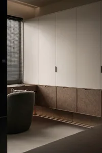 A modern minimalist bedroom featuring a sleek storage system with light and dark wood finishes, and a comfortable upholstered