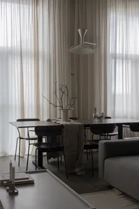 A minimalist residential setting featuring a wooden table, a white lamp, and sheer curtains, with a cozy ambiance.
