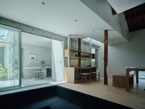 A modern living room with a concrete ceiling and floor, featuring a mid-century modern sofa, a kitchen island with a round wo