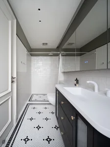 Modern bathroom with white tiles and a black pattern floor, white vanity, and mirror above the sink.