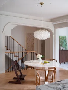 Modern dining room with a marble table and chairs, featuring a round chandelier and white curtains.