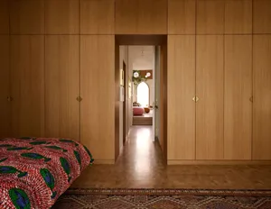 A minimalist bedroom with a bed featuring a red and green patterned blanket placed on a wooden rug.