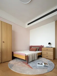 A minimalist bedroom with a circular rug, wooden furniture, and a pink headboard and blanket.