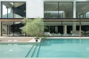 Modern residential poolside area featuring glass walls and a hanging chair.