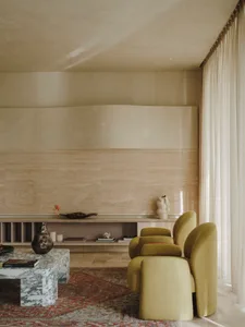 A living room with minimalist design, featuring marble accents, fabric furniture, glass elements, and wooden finishes.