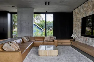 A modern living room with a sectional leather sofa, concrete walls, and a stone fireplace.