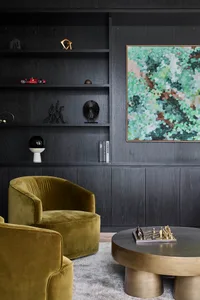 A modern living room featuring dark wooden walls and furniture, a round table with a chessboard, and a large abstract paintin