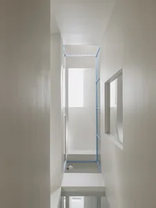 A minimalistic white corridor with concrete walls and a grid ceiling design.