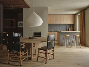 A modern residential kitchen featuring a wooden dining table, black and wooden chairs, a wooden kitchen counter, and a pendan