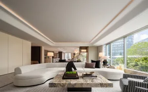 Spacious modern living room featuring a curved white sofa with accent cushions, a marble coffee table, and a large window ove