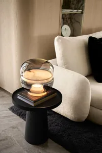 A modern minimalist living room featuring a glass light fixture on a small round wooden side table, with a creamy sofa and bl