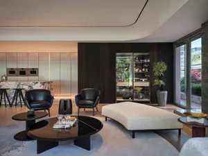 A modern residential lobby features contemporary furniture, a glass display cabinet, and a large window overlooking an outdoo