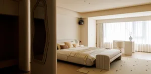 A minimalist bedroom featuring a bed with fabric bedding, a soft, cushioned bench at the foot, and a large window with sheer 