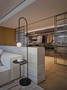 A modern bedroom featuring a bed with a white headboard, a side table with a black lamp and a cup of coffee, and a closet wit