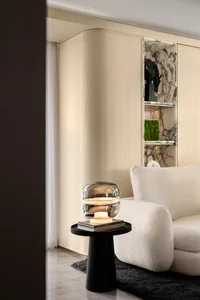 A modern living room with minimalist furniture, a sleek lamp, and a wall-mounted shelf displaying decorative items.
