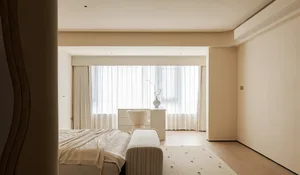 A minimalist bedroom with neutral tones and soft textiles, featuring a large bed, a small bench, and a simple desk with a vas