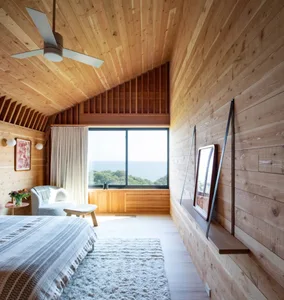 A minimalist bedroom featuring wood paneling, a large window with a view, and a cozy seating area.