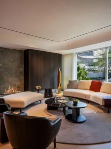 Modern living room with a neutral color palette featuring a curved sofa, ottoman, and coffee tables with decorative items.