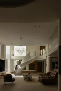 A modern minimalist living room featuring a white staircase, pendant chandelier, and minimalist furniture.