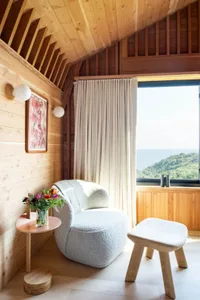 A cozy, minimalist living room with a cozy, white, plush armchair adorned with white cushions nestled in a cozy nook, illumin