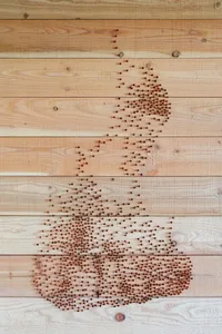 A piece of industrial-style string art made from wooden beads arranged on a wooden surface to form the shape of a coffee cup 