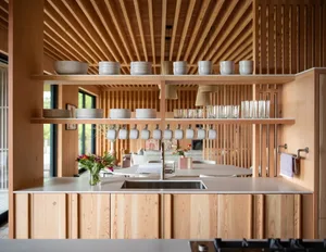 A modern kitchen with rustic wooden cabinets, open shelving displaying white dinnerware, and a sleek sink area.