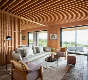 Modern living room featuring wooden slatted ceiling, plush grey sofa, and pink and wood furniture.