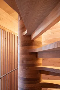 Modern wooden spiral staircase with light-colored wood panels and railing.