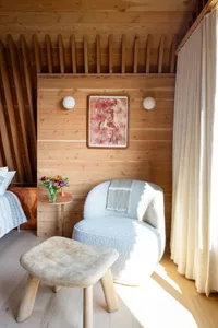 A modern residential interior showcasing wooden walls, a cozy armchair, and a small round table with flowers and a vase.