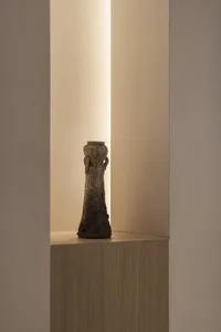 A ceramic vase with an industrial style design sits on a wooden pedestal in a minimalist setting.