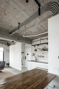 Modern residential kitchen featuring concrete and metal pipes, a wood countertop, and white walls.
