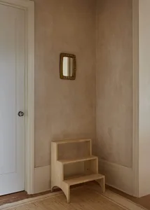Minimalist interior design featuring a wooden shelf with a small mirror on the wall and a white door.