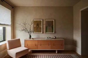 Minimalist residential room featuring concrete surfaces, a pink armchair, and a wooden cabinet.