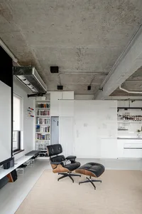 Industrial-style living space with concrete ceiling, minimalist furniture, and open kitchen area.