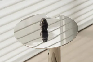 A modern metal sculpture depicting an owl on a reflective tabletop.