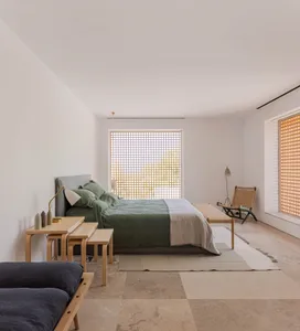 A minimalist bedroom featuring wooden furniture and light-colored bedding with a view of nature through the window.