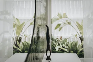 A minimalist metal sculpture on a white table in a well-lit room with green plants and white curtains.